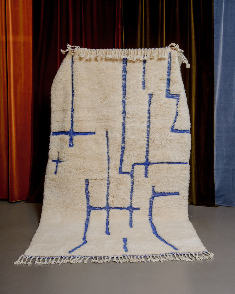 Cream and blue Berberlin Finest rug being held up in front of velvet curtains.