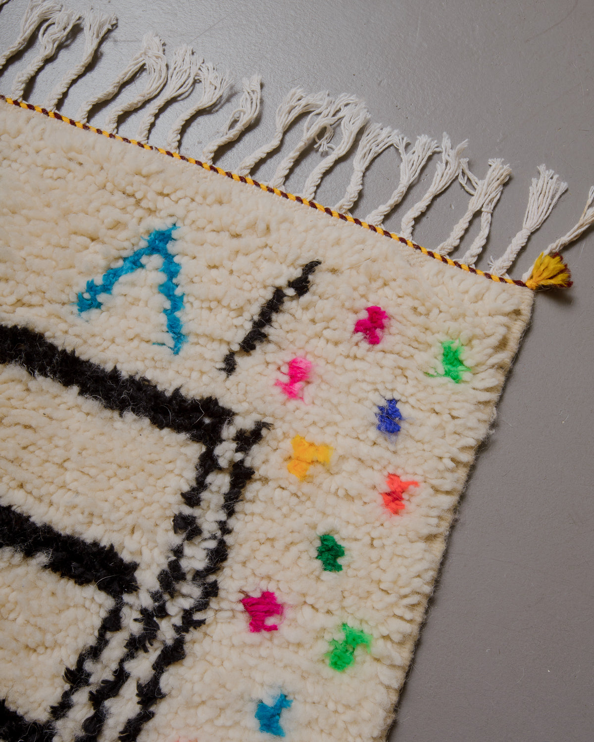 Corner of azilal rug with white cotton tassels.