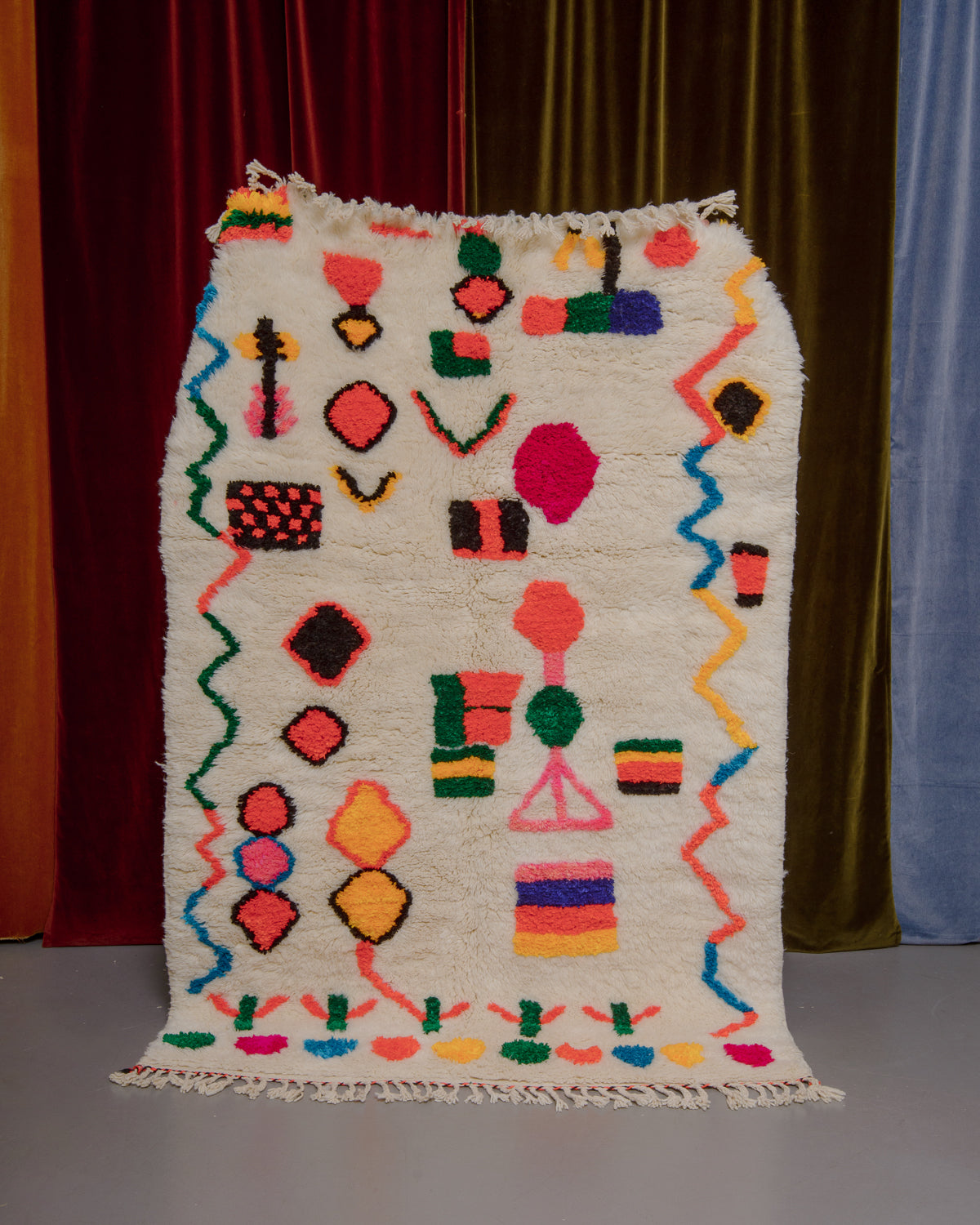 Berberlin Finest rug with a heavy cream pile and colourful design in cotton being held in front of velvet curtains. 