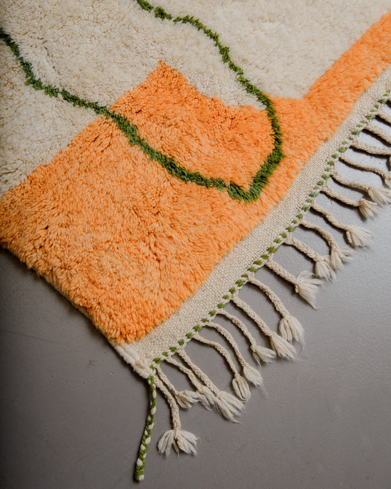 Corner of rug with orange, green and cream wool and natural wool tassels.