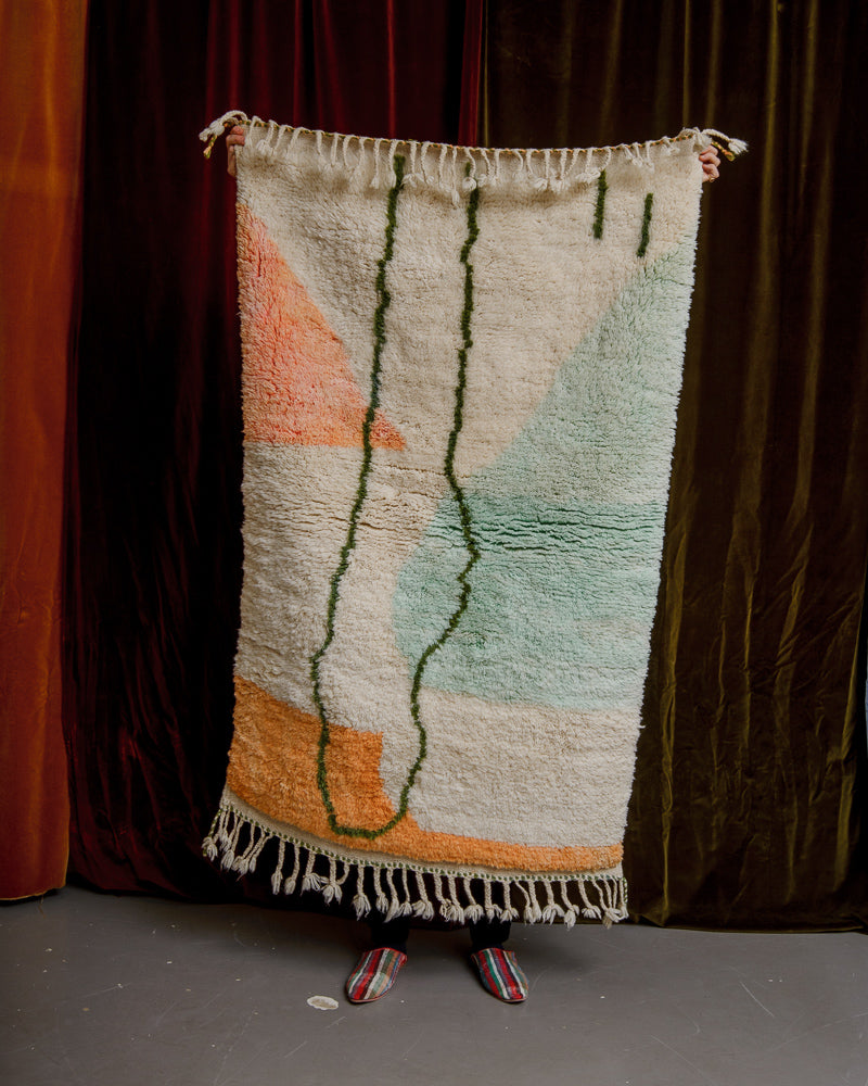 wool rug being held up in front of velvet curtains.