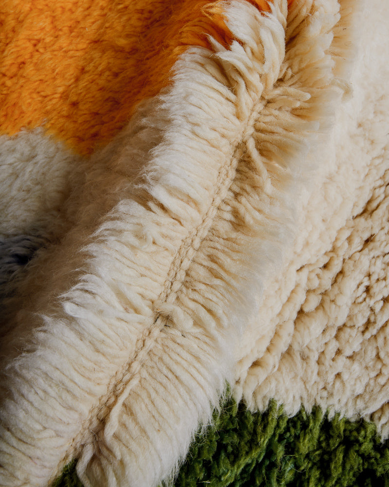 Close up of wool rug with thick pile in green, yellow and cream.