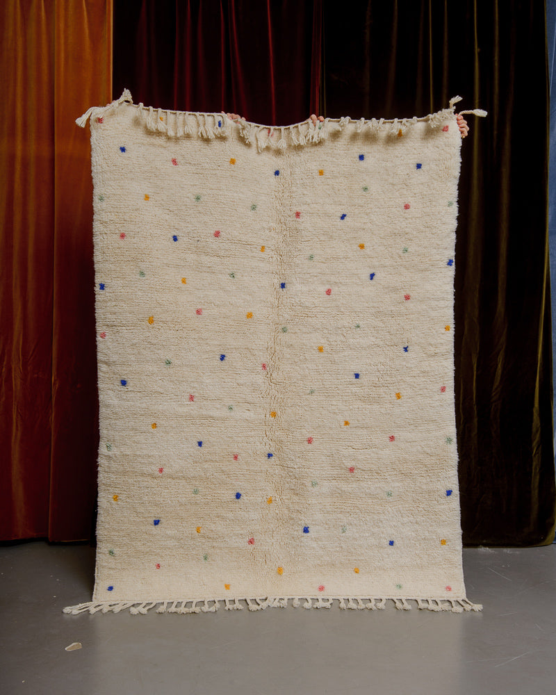 Cream wool rug with colourful polka dots in front of velvet curtains.