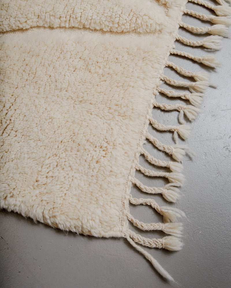 Corner of wool rug with tassels on grey floor. 