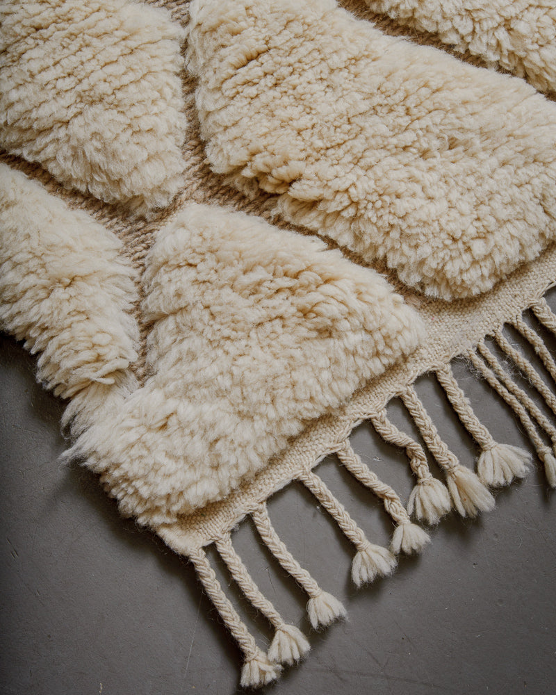 Corner of wool rug with tassels on grey floor. 