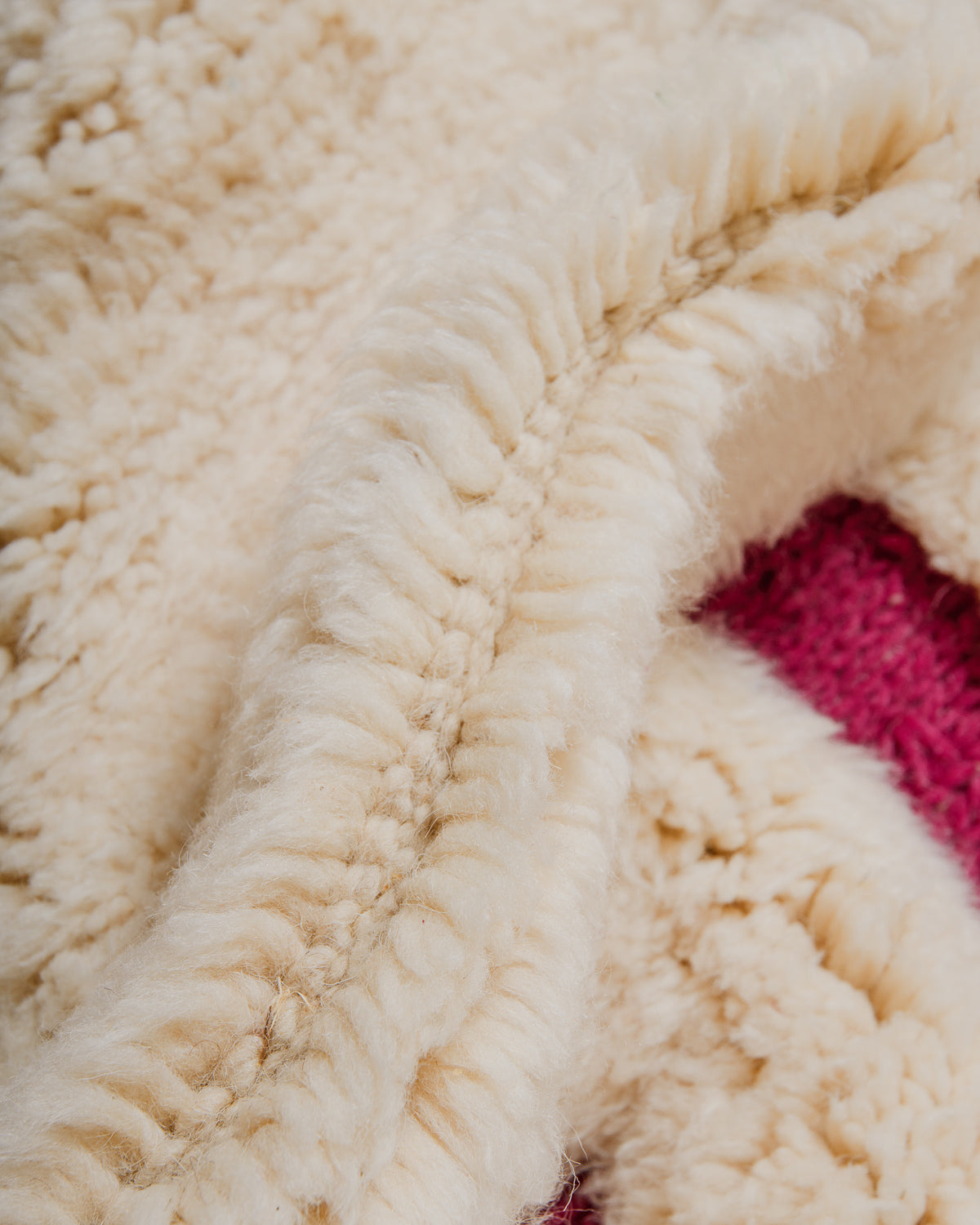 Close up of cream and magenta rug with thick pile and woven areas. 