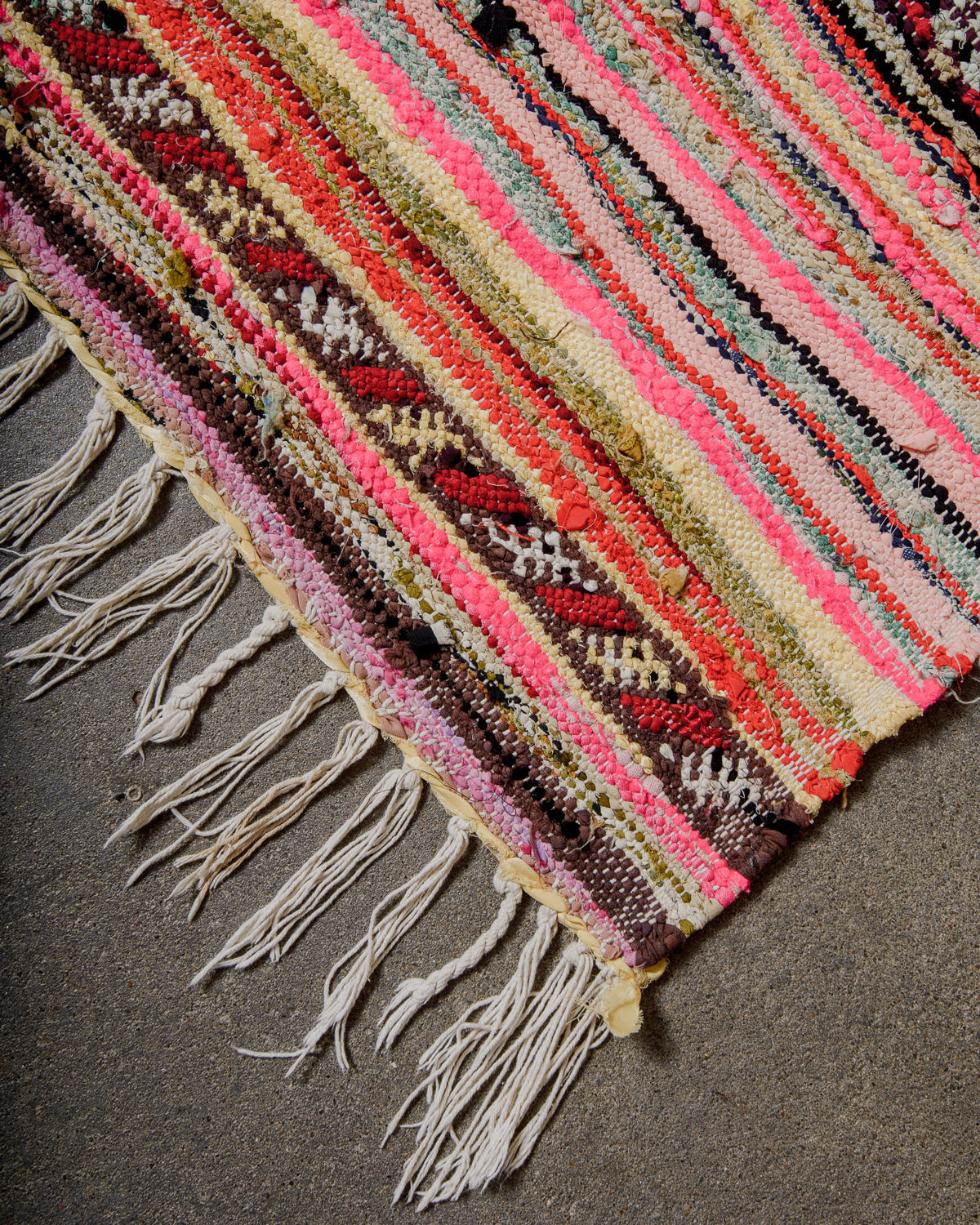 Corner or kelim rug made of fabric remnants in warm shades of red, pink, pale yellow and brown.