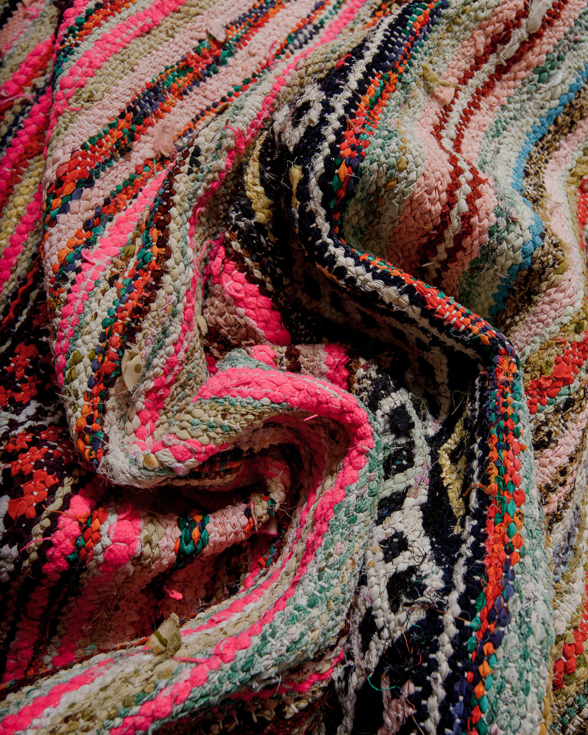 Close-up of a colourful textured fabric rug with pink, black, and multicolour patterns.