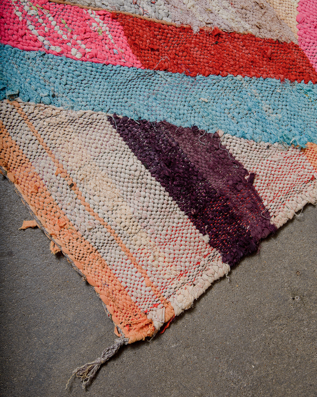 Corner of woven boucherouite rug with recycled cloth remnants in various colours and patterns.