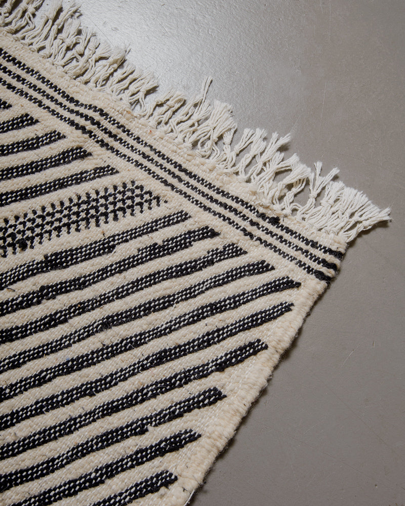 Corner of kelim rug with white cotton tassels.