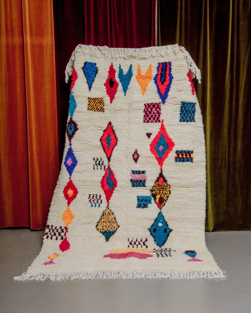 Colourful azilal rug held in front of velvet curtains. 