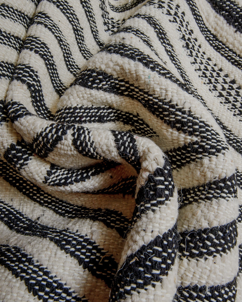 Embroidered surface of kelim rug made of cream and black wool and white cotton stitching.