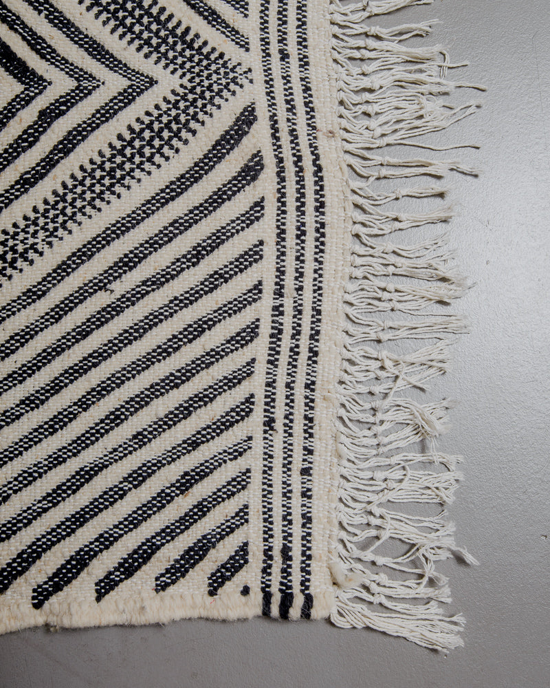Corner of black and white Kelim rug with white cotton tassels. 