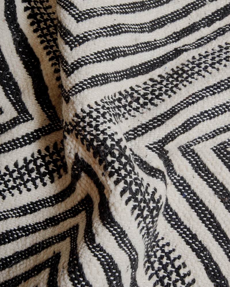 Embroidered surface of kelim rug made of cream and black wool and white cotton stitching.