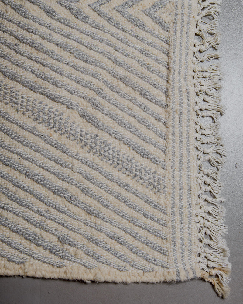 Corner of kelim rug with white cotton tassels.