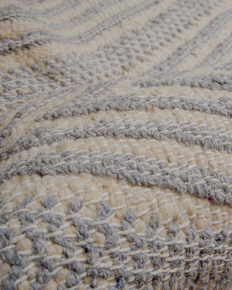 Embroidered surface of kelim rug made of cream and light grey wool and white cotton stitching.