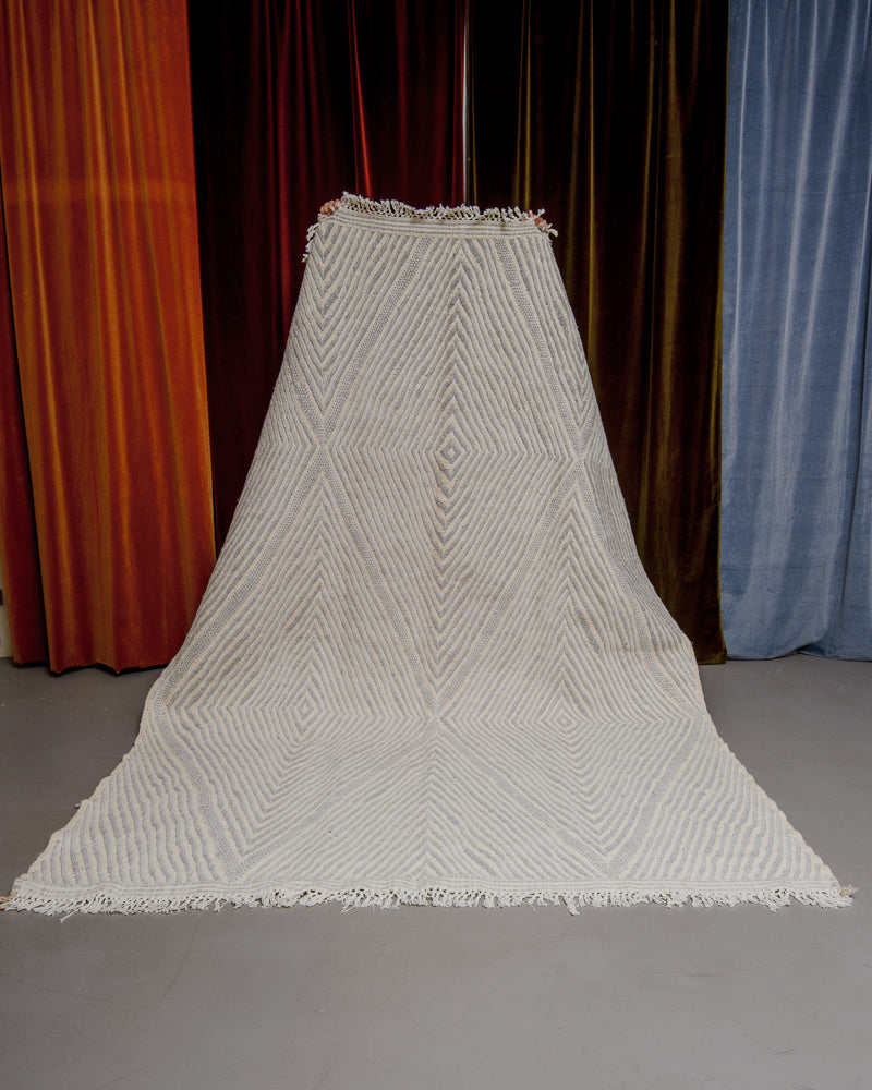 Grey and white kelim rug held up in front of velvet curtains