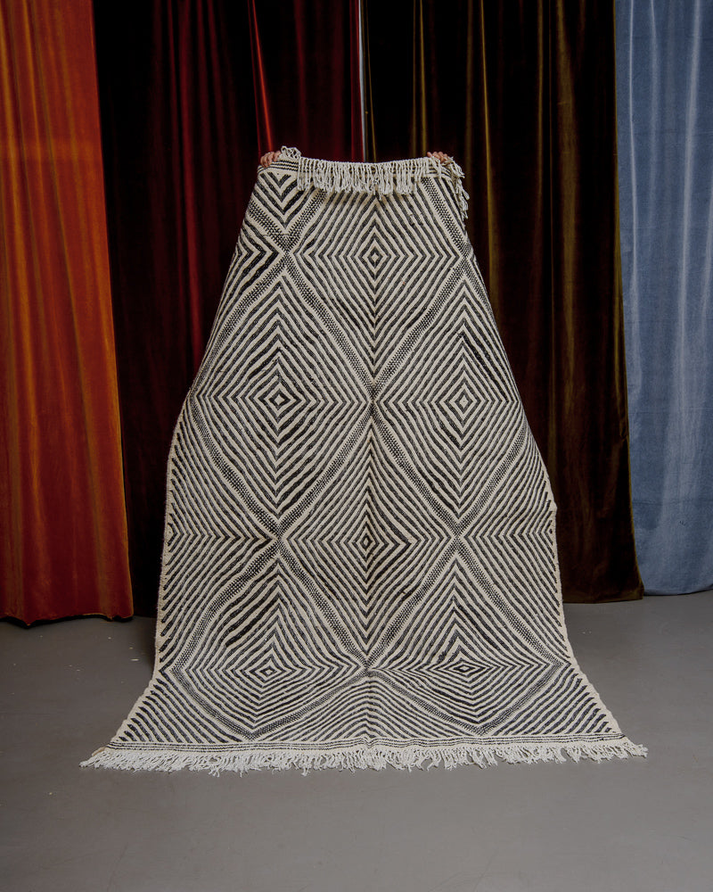 Black and white Berberlin kelim rug held up in front of velvet curtains.