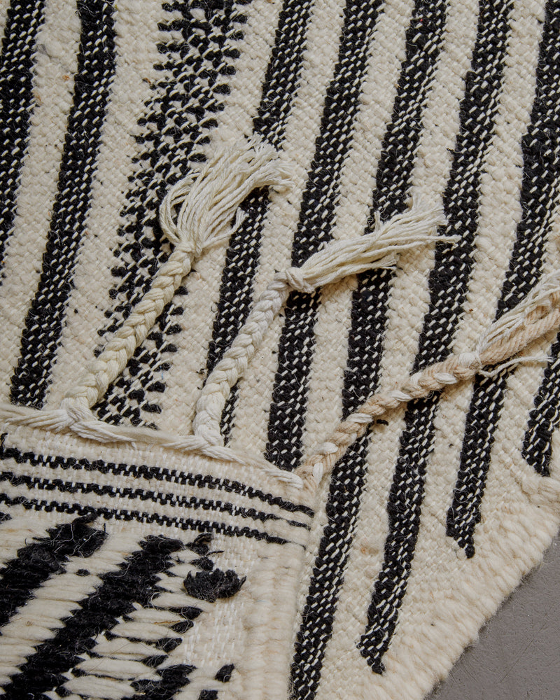 Corner of kelim rug with cotton tassels in various shades of white.