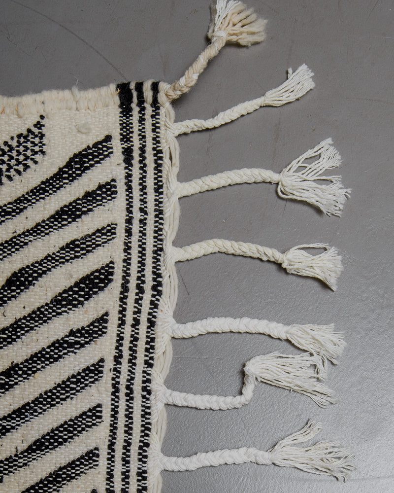 Corner of kelim rug with cotton tassels in various shades of white.
