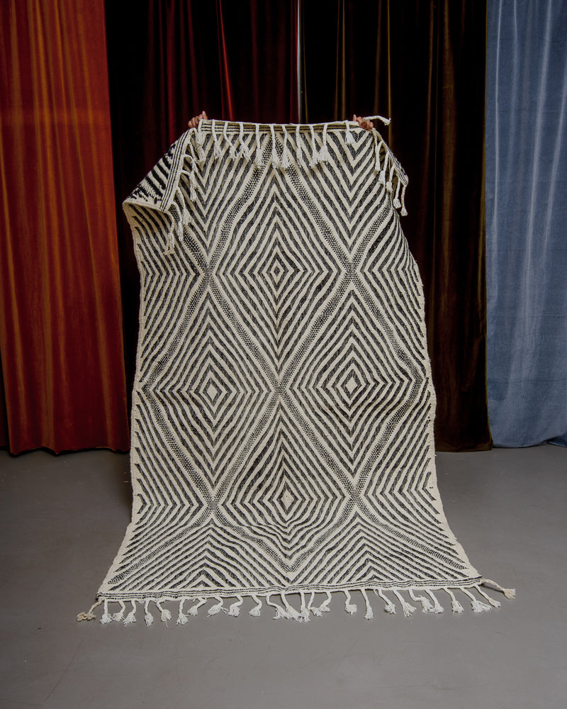 Black and white Berberlin kelim rug held up in front of velvet curtains.