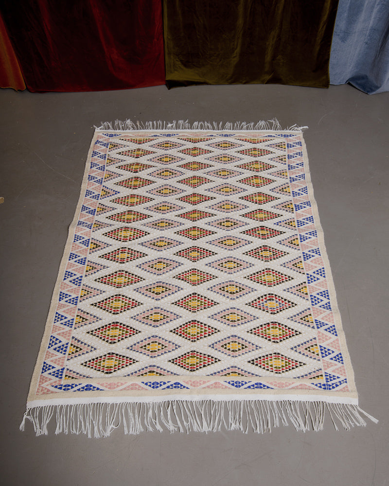 Kelim rug with diamond pattern on grey floor.