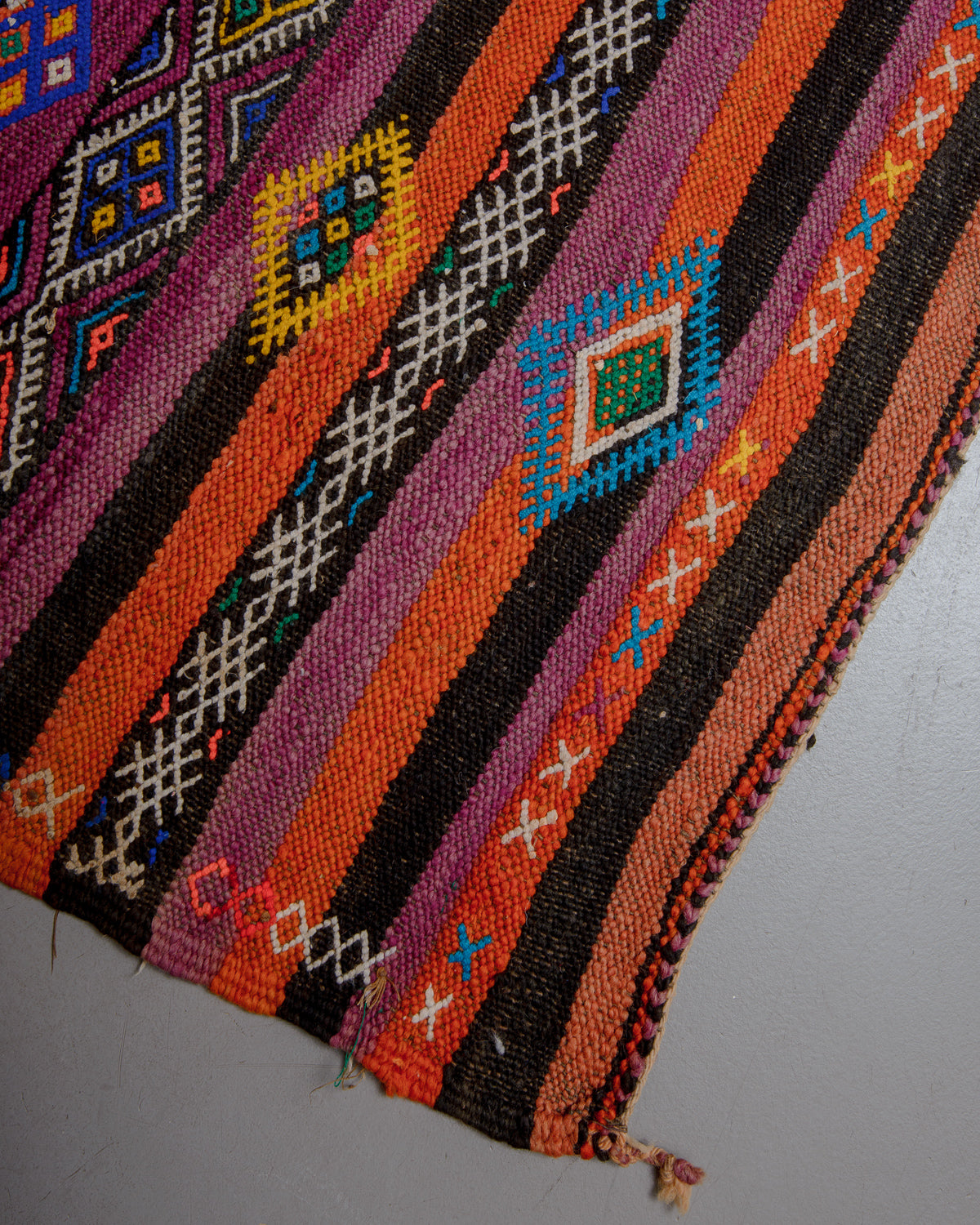 Corner and edge of vintage kelim in orange, mauve, blue, yellow and black.