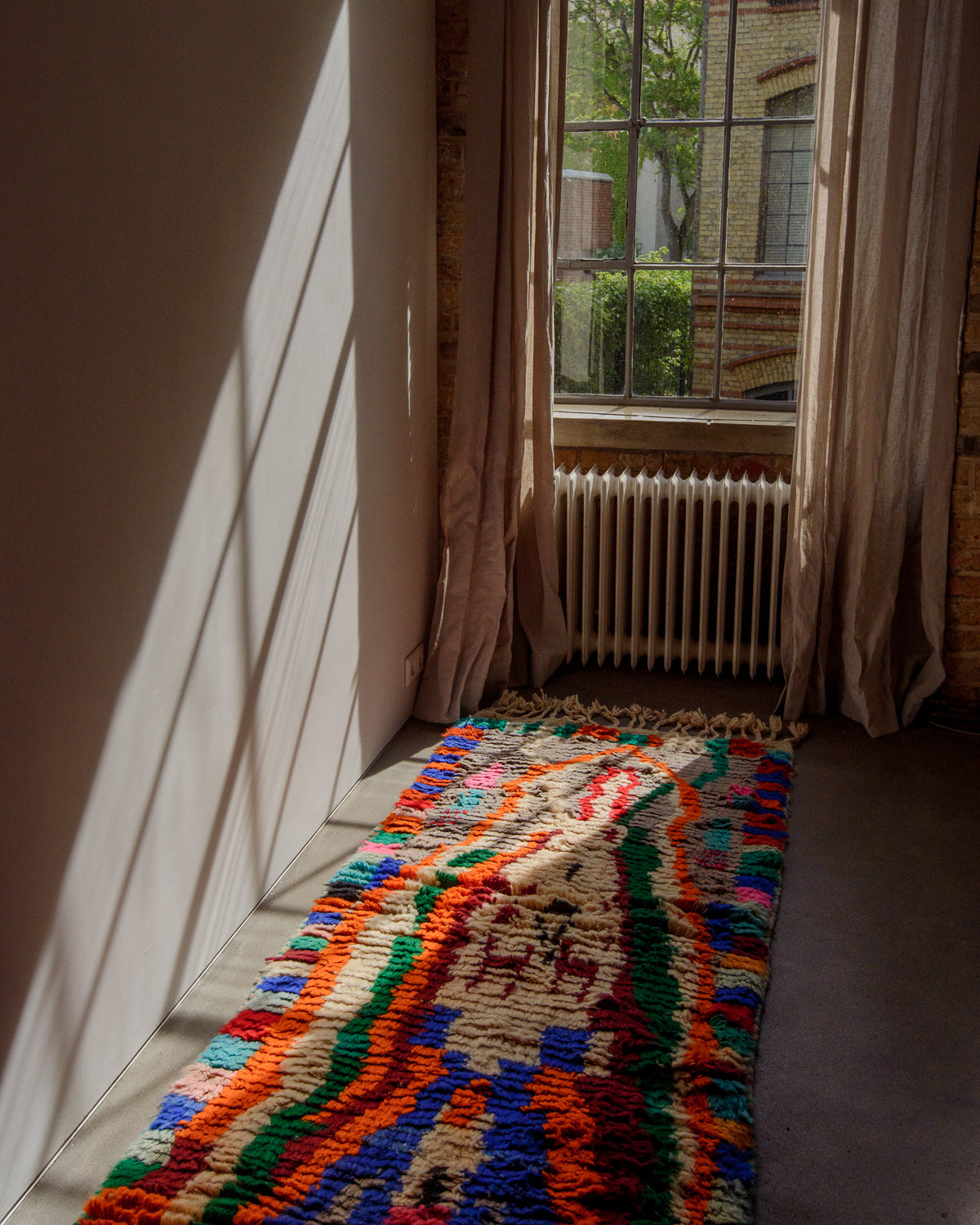 Colourful Berberlin runner rug laying in front of a window with sunlight streaming in.