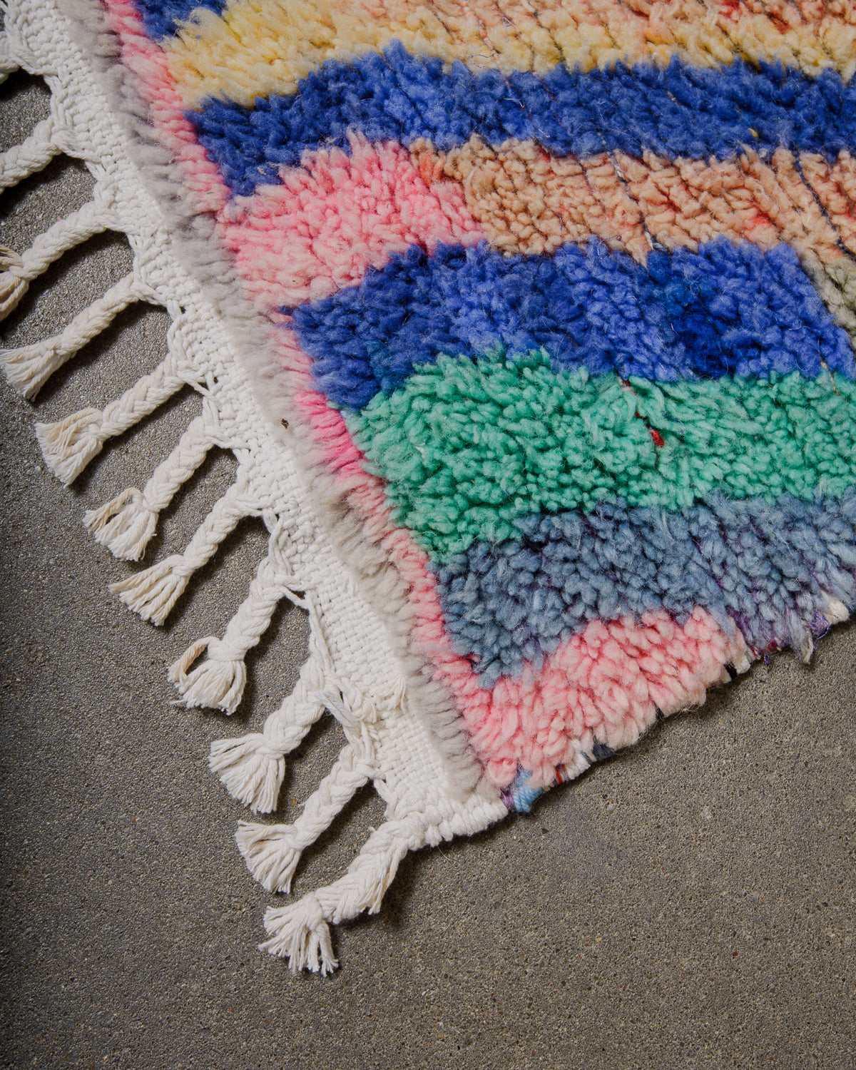 Multicoloured wool rug with tassels on a cement surface
