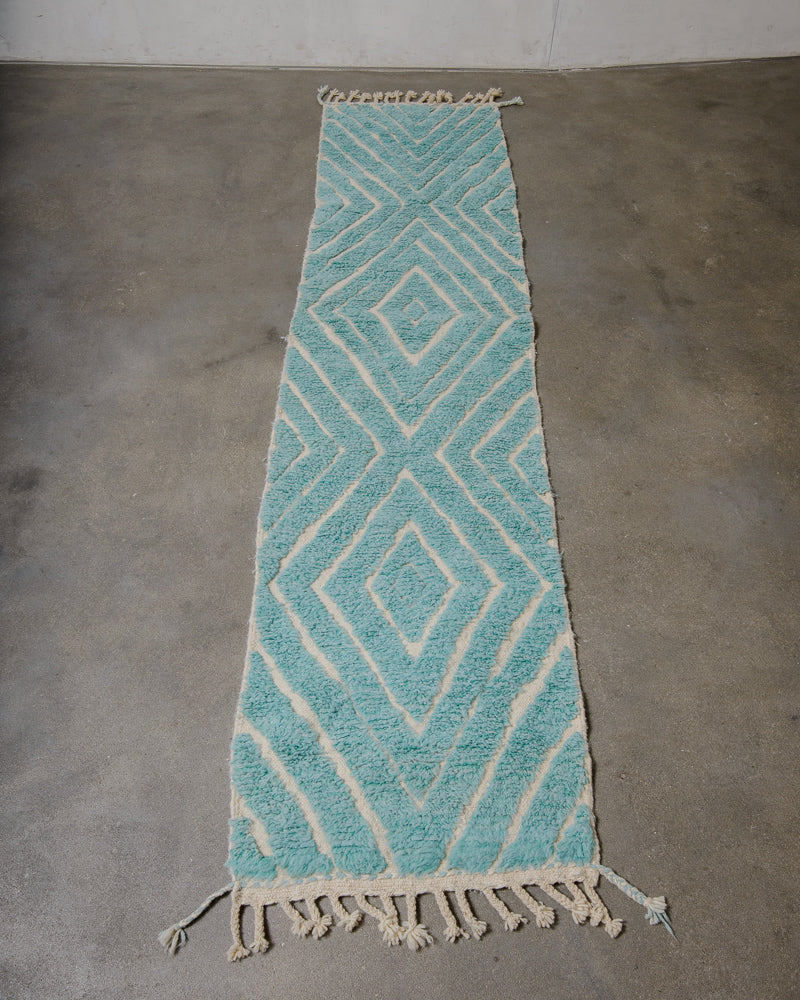 Turquoise and beige geometric patterned rug on a concrete floor