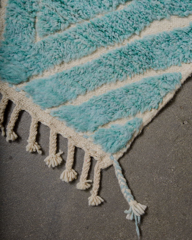 Turquoise and cream textured rug with tassels on a dark surface
