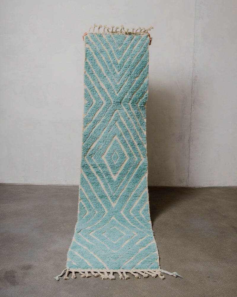 Turquoise geometric patterned rug on a gray floor with a plain wall background