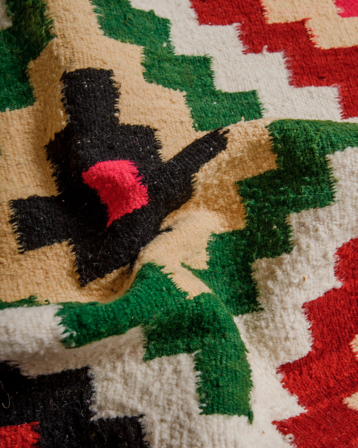 Close-up of a patterned fabric with geometric shapes in black, green, and red on a beige background.