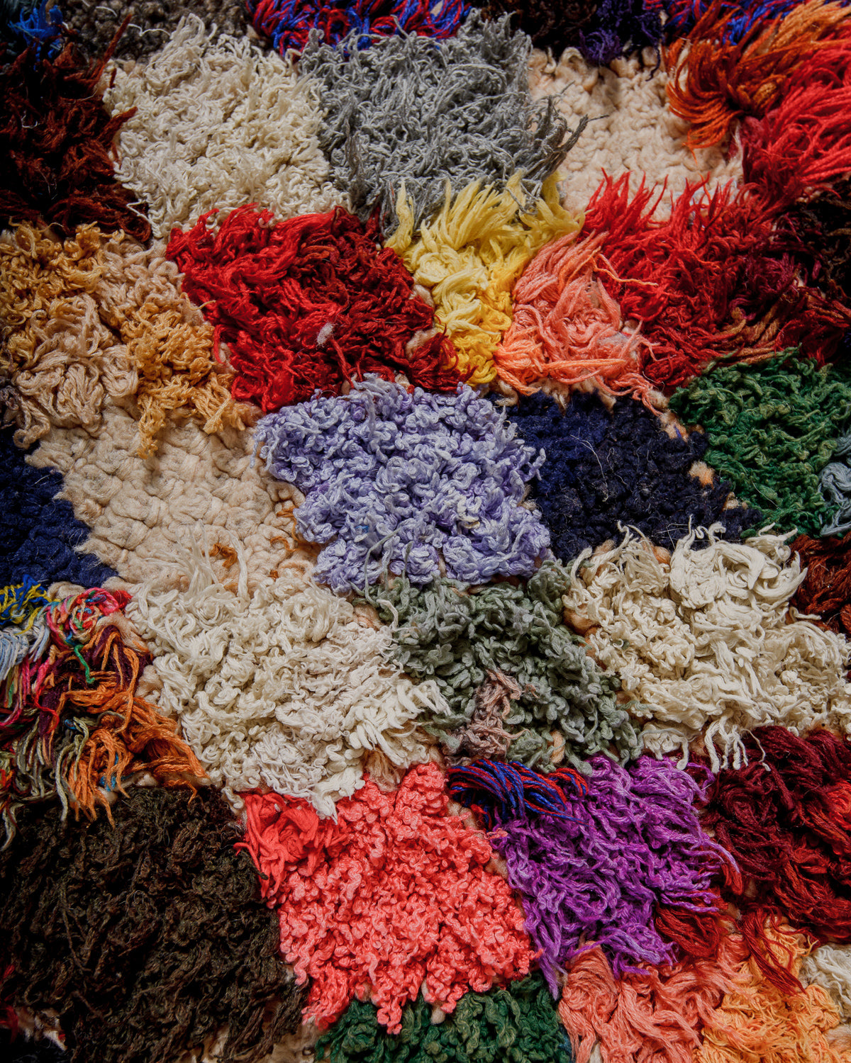 Multicoloured textured yarn rug surface with various colours including red, yellow, blue, green, and purple.