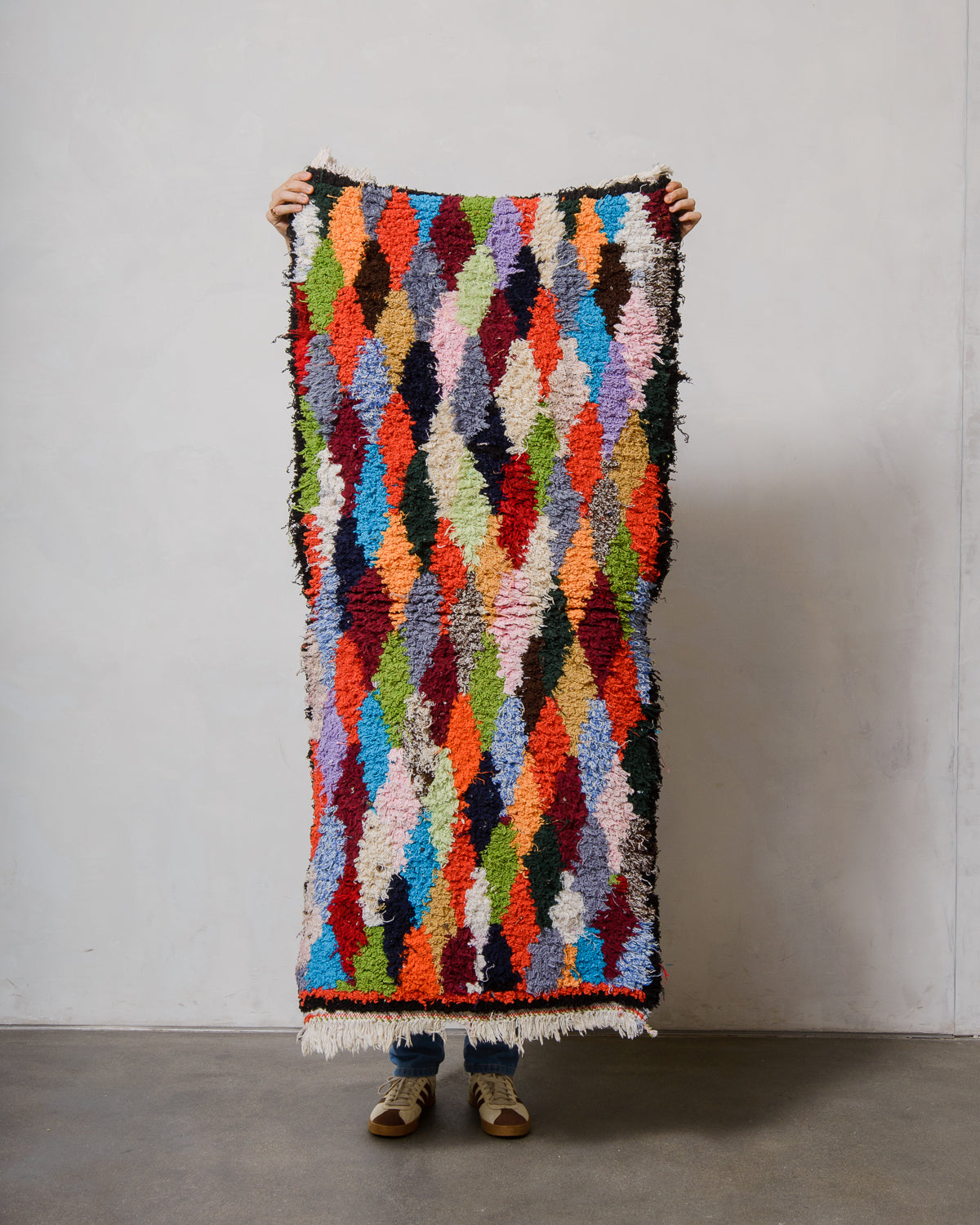 Person holding a colourful textured rug against a plain background