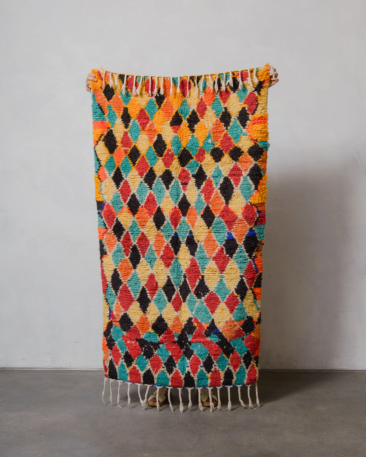 Colorful diamond patterned rug with fringe on a plain background