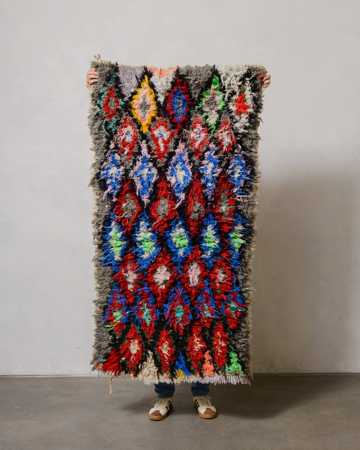 Person holding a colorful patterned rug against a plain background