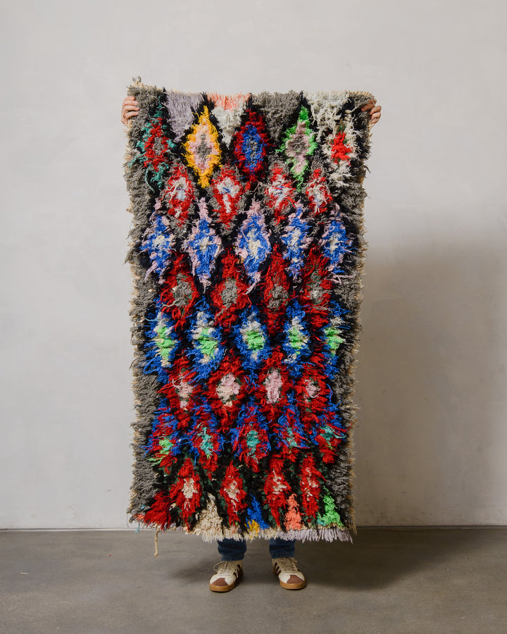 Person holding a colorful patterned rug against a plain background