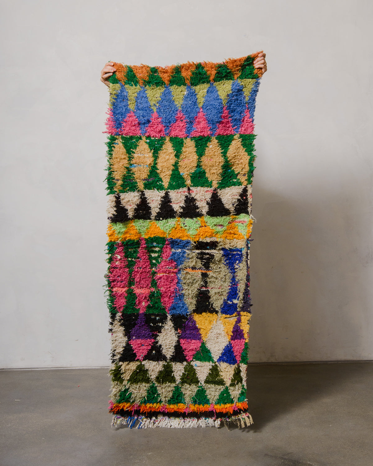 Colorful woven rug with geometric pattern held by a person against a plain background