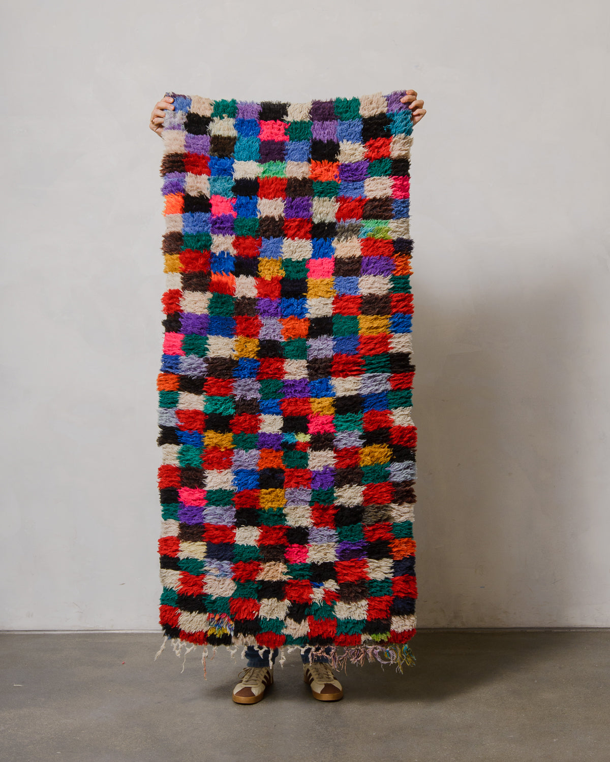 Multicolored checkered rug held by a person against a plain background