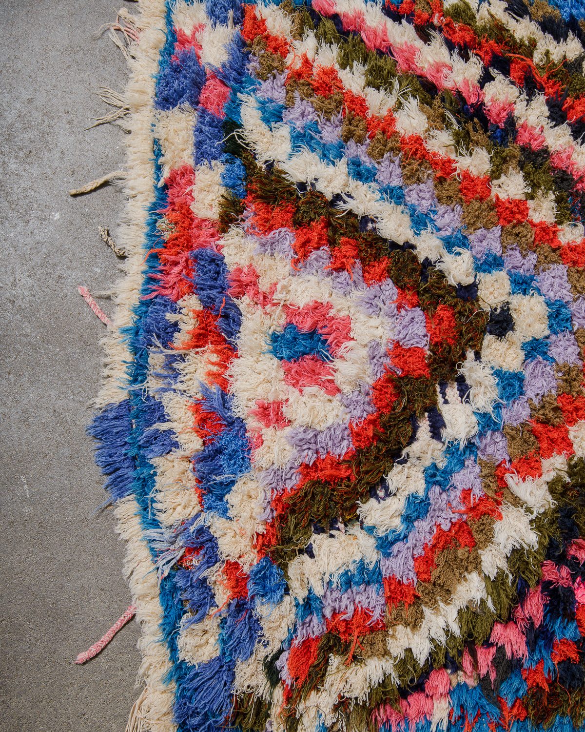 Edge of Berberlin vintage Boucherouite runner displaying randomly placed cotton tassels in pink and white.