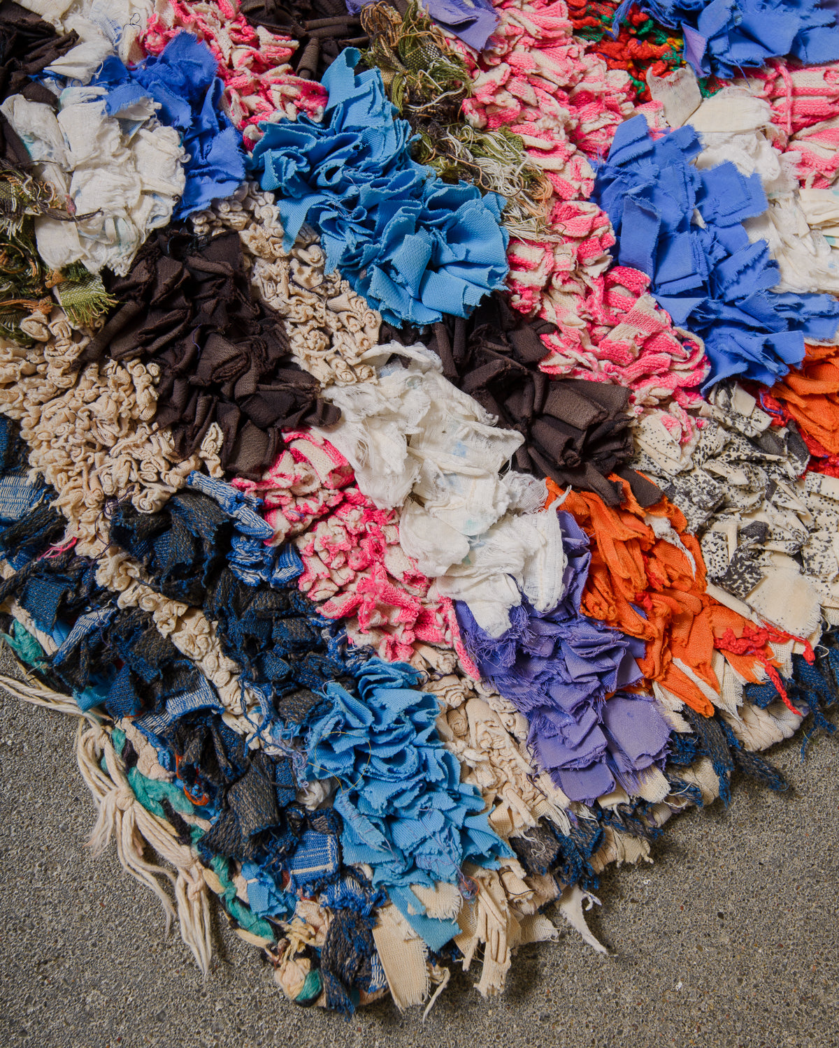 Colorful woven rug with various fabric pieces on a concrete surface