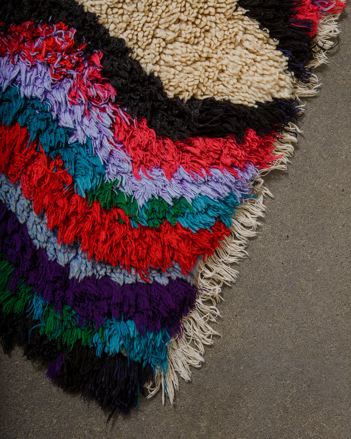 Multicolored textured rug with fringe on a concrete floor