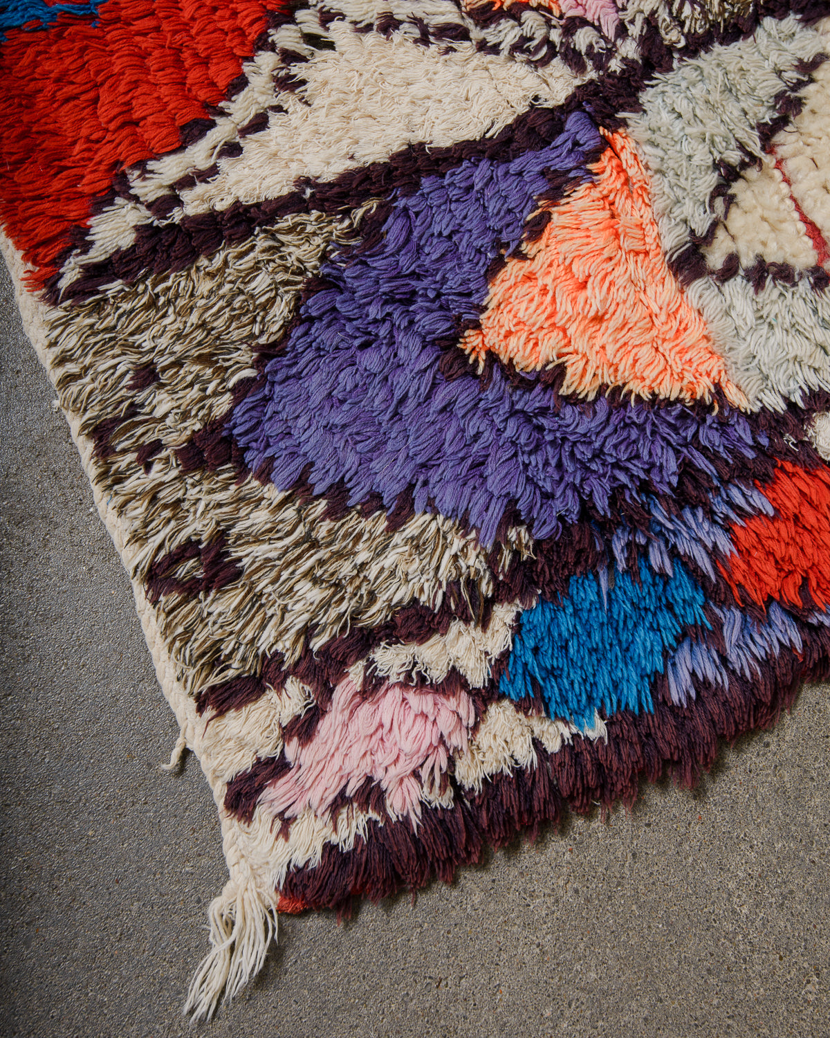 Colorful geometric patterned rug with fringes on a gray floor.