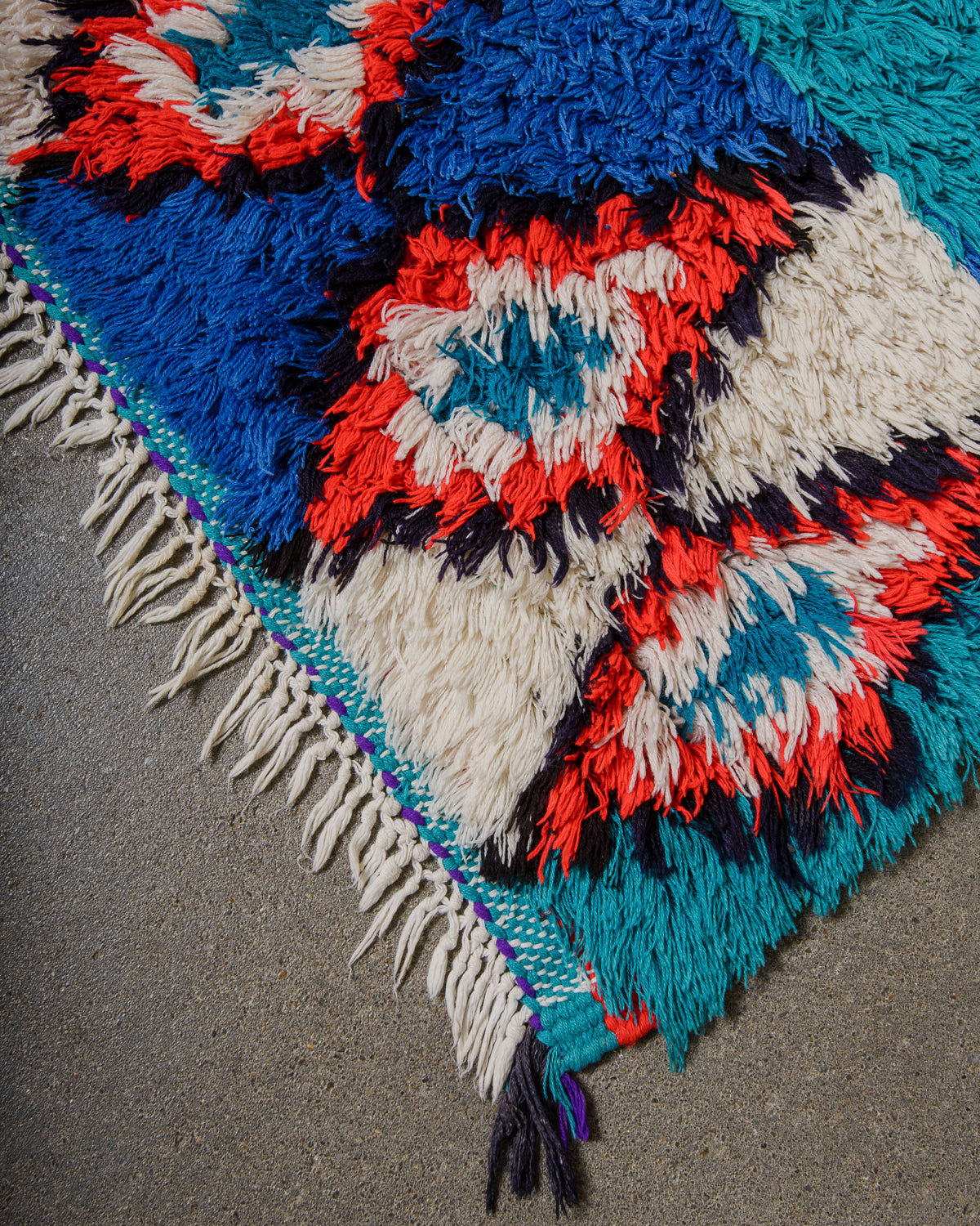 Corner of woven rug with geometric pattern on a grey surface