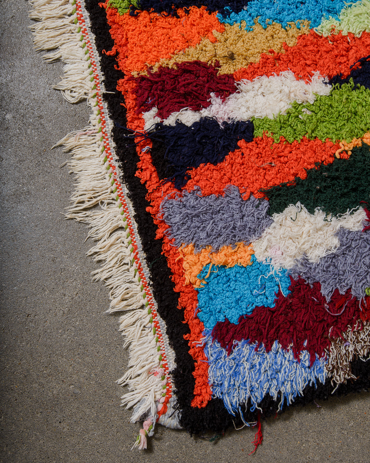 Colourful woven rug with fringe on a concrete floor