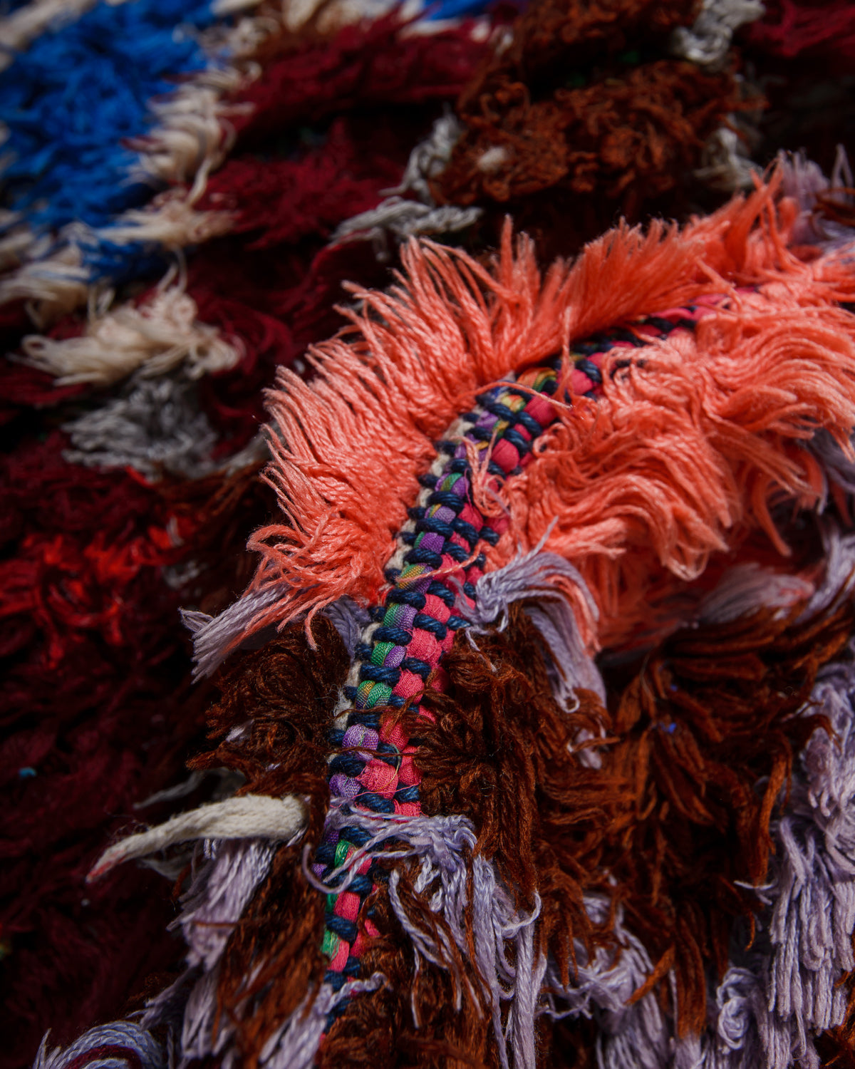 Close-up of a textured rug with colourful threads and fringes.