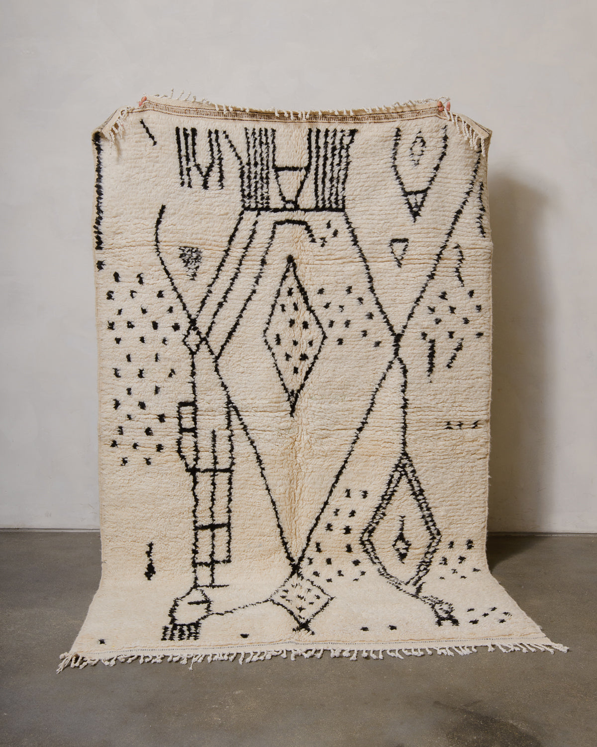 Berberlin Azilal rug made of fluffy cream wool and black design, held up in front of a plain background.