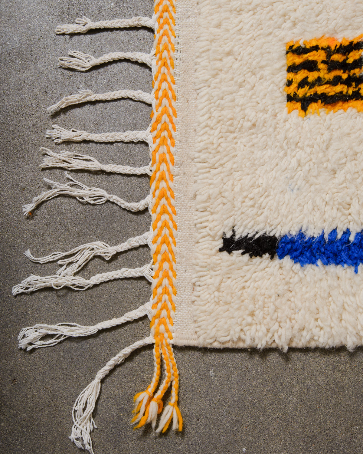 Corner of Azilal rug with white cotton tassels and bright, yellow weaving across the edge.