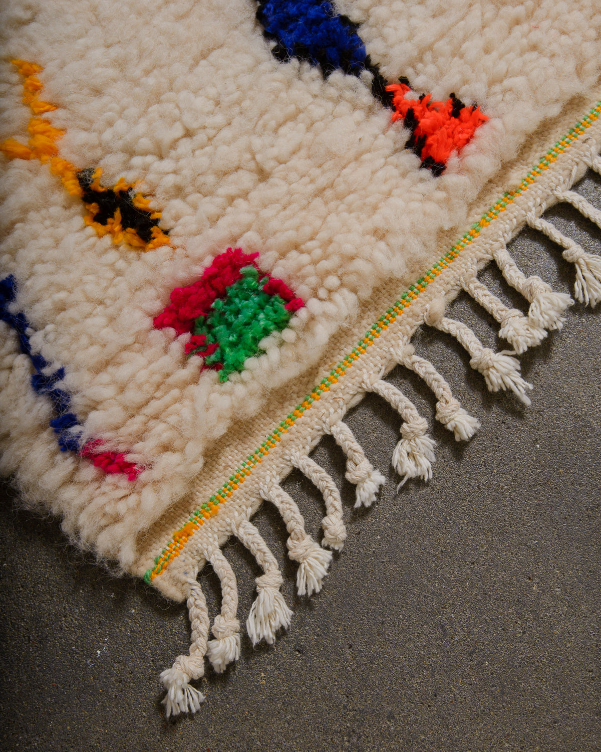 Corner of Azilal rug with a tightly woven edge and white cotton tassels along the end.